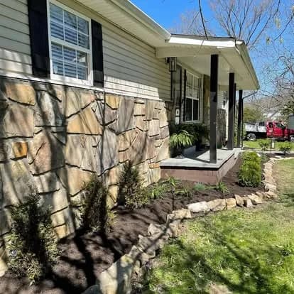 Landscaped front yard of a house featuring a stone facade and newly planted foliage.